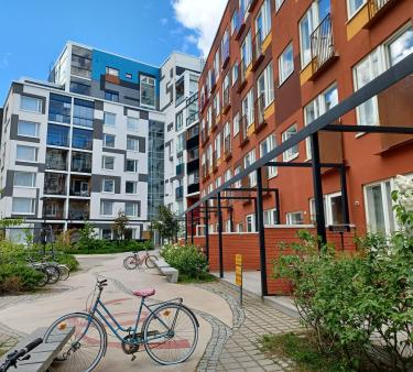 Hoasin vuokratalon vehreää piha-aluetta Helsinkin Jätkäsaaressa. Kuvassa oikealla Hoasin talon punaruskeaa seinustaa, sen takana valkoinen naapuritalo.