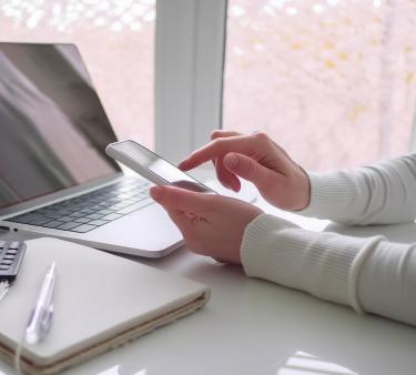 Tekoälyllä teetetty kuvituskuva, jossa henkilö kannettavan tietokoneen ja puhelimen äärellä.