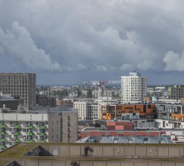 Rakenteilla olevan Helsingin Jätkäsaaren maisemaa talojen kattojen tasalta. Talojen lomassa nostokurkia. Helsingin kaupunkisiluettia etualalla olevan Jätkäsaaren taustalla.